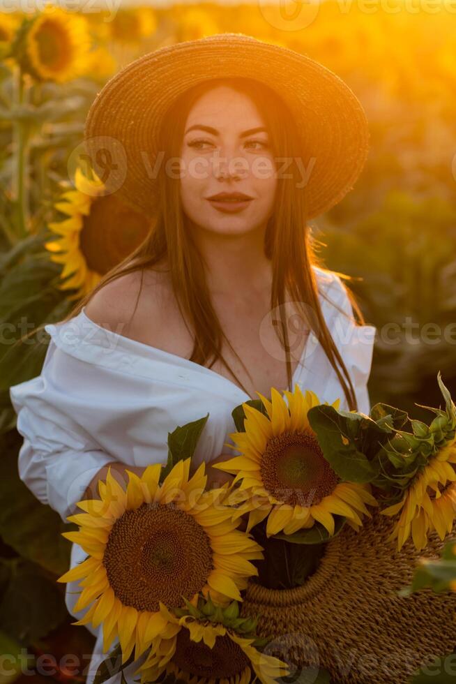 ein Mädchen im ein Hut auf ein schön Feld von Sonnenblumen gegen das Himmel im das Abend Licht von ein Sommer- Sonnenuntergang. Sonnenstrahlen durch das Blume Feld. natürlich Hintergrund. foto