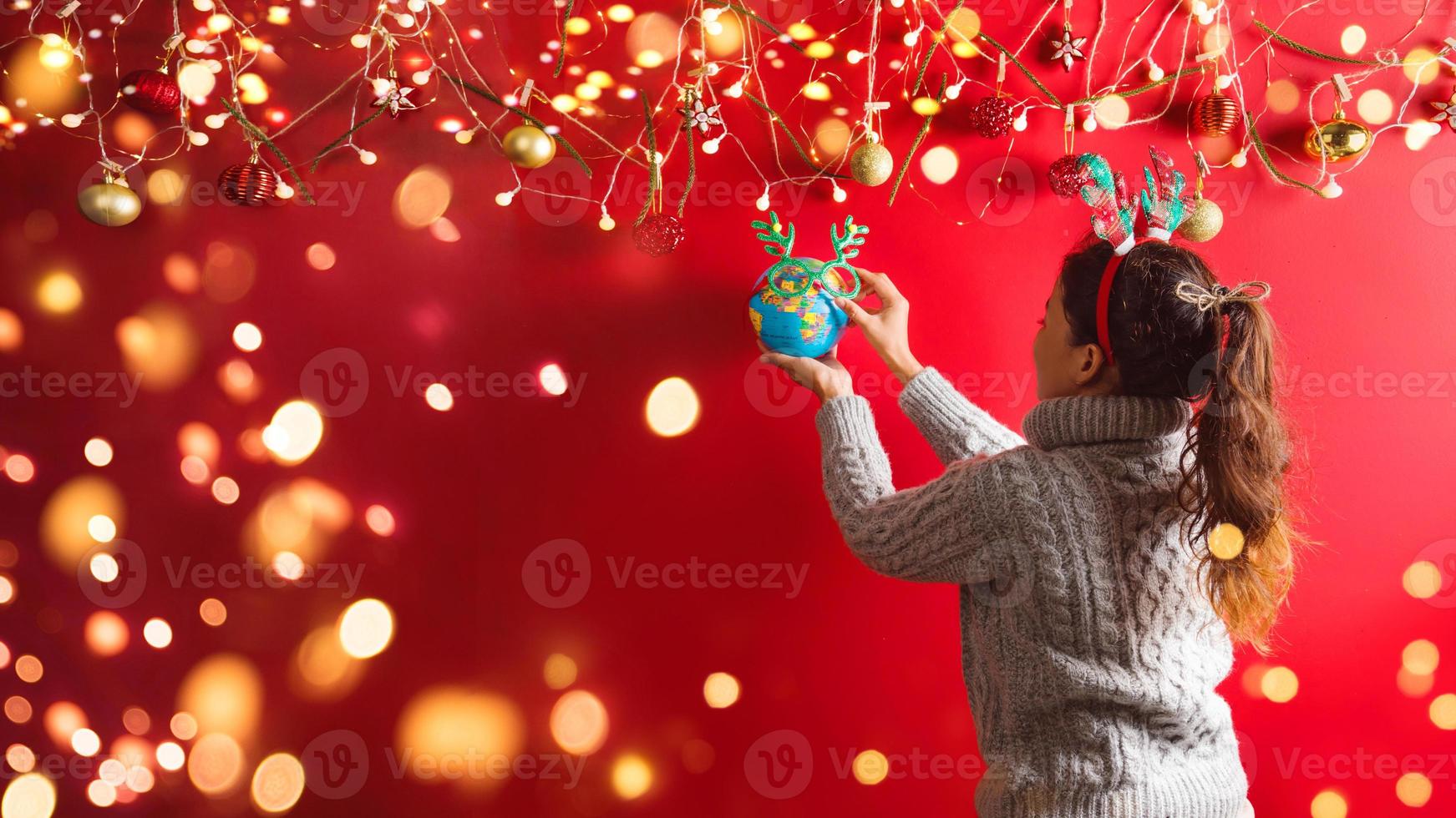 Frohe Weihnachten und ein glückliches neues Jahr. Das Mädchen gestaltet mit Weihnachtsschmuck Dekoration. der weihnachtshintergrund rot. mit Kopienraum für Ihren Text. LED Lichter foto