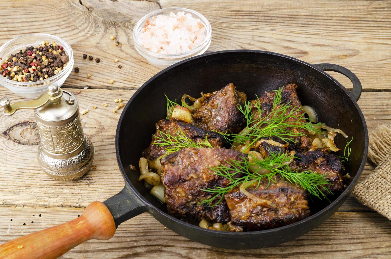 Gusseiserne Pfanne auf Holztisch mit gebratener Leber. foto