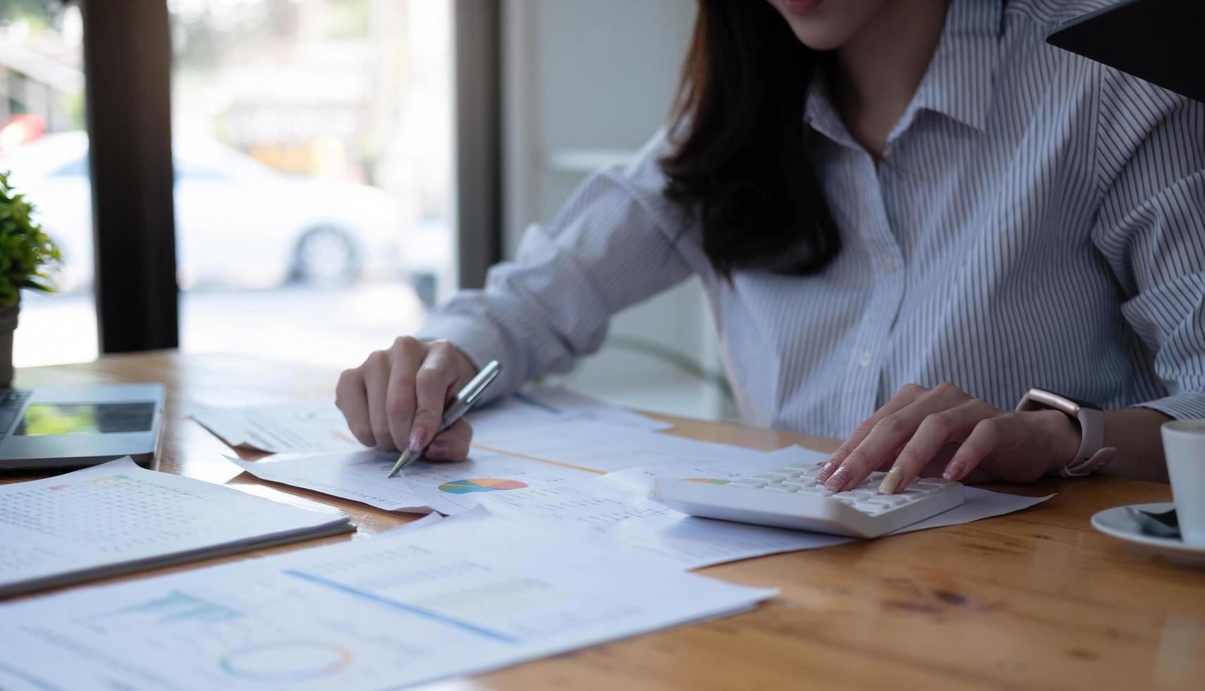 asiatische Frau mit Finanzbericht und Taschenrechner. Frau mit Taschenrechner, um Bericht am Tisch im Büro zu berechnen foto