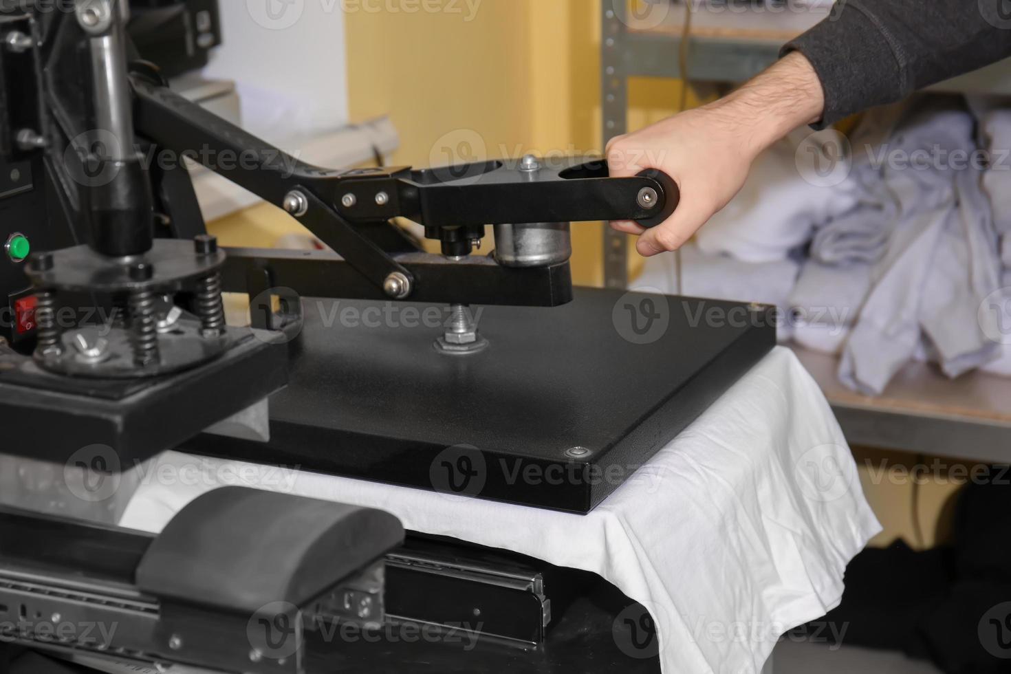 junger Mann druckt auf T-Shirt in der Werkstatt foto