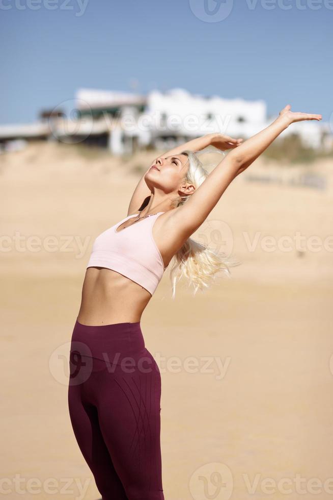 Kaukasische blonde Frau, die Yoga am Strand praktiziert foto