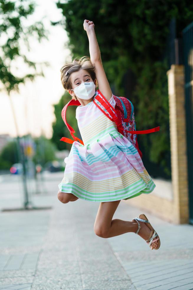 Mädchen, das eine Maske trägt, macht einen Sprung vor Freude über die Rückkehr zur Schule. foto