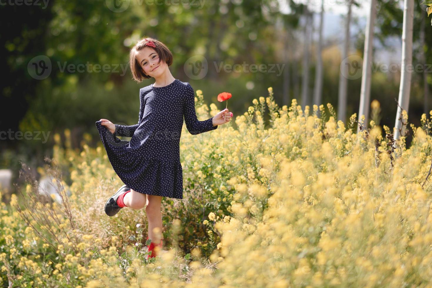 kleines Mädchen, das auf dem Naturfeld spazieren geht und ein schönes Kleid trägt foto