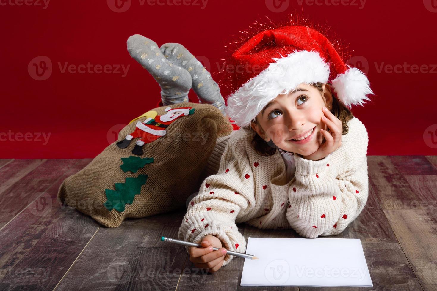 entzückendes kleines Mädchen mit Weihnachtsmütze, das einen Weihnachtsbrief schreibt foto