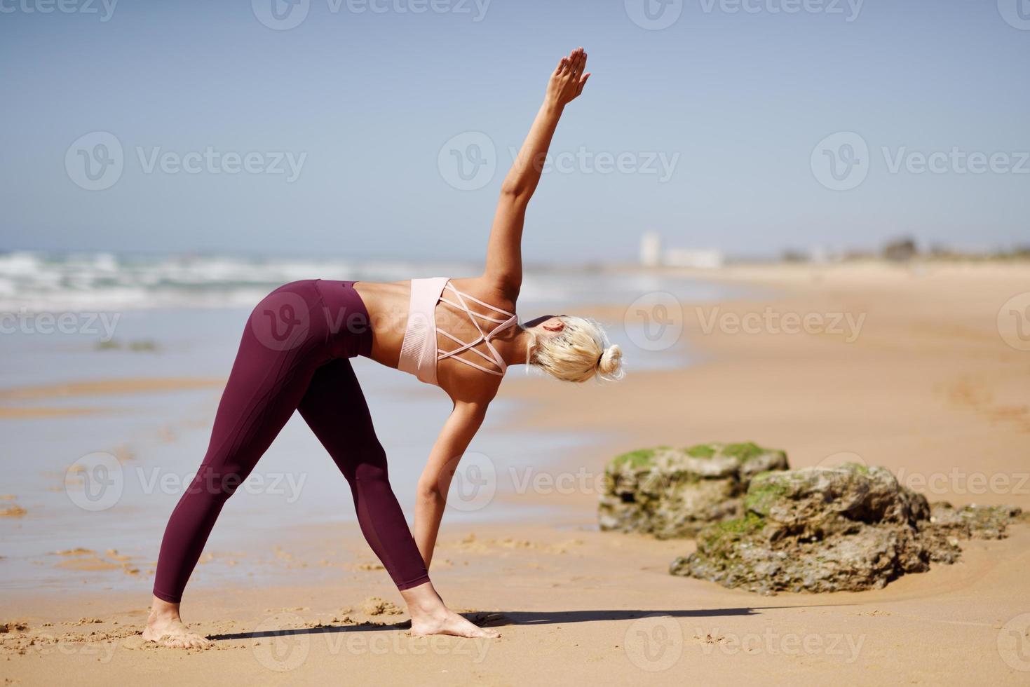 Kaukasische blonde Frau, die Yoga am Strand praktiziert foto