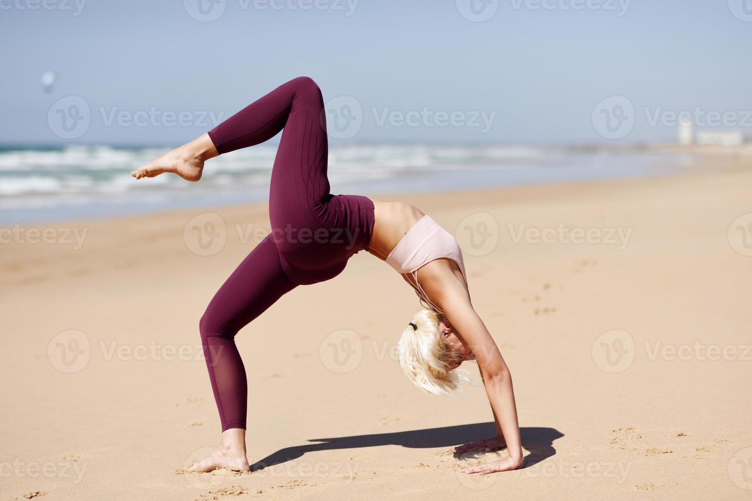 Kaukasische blonde Frau, die Yoga am Strand praktiziert foto