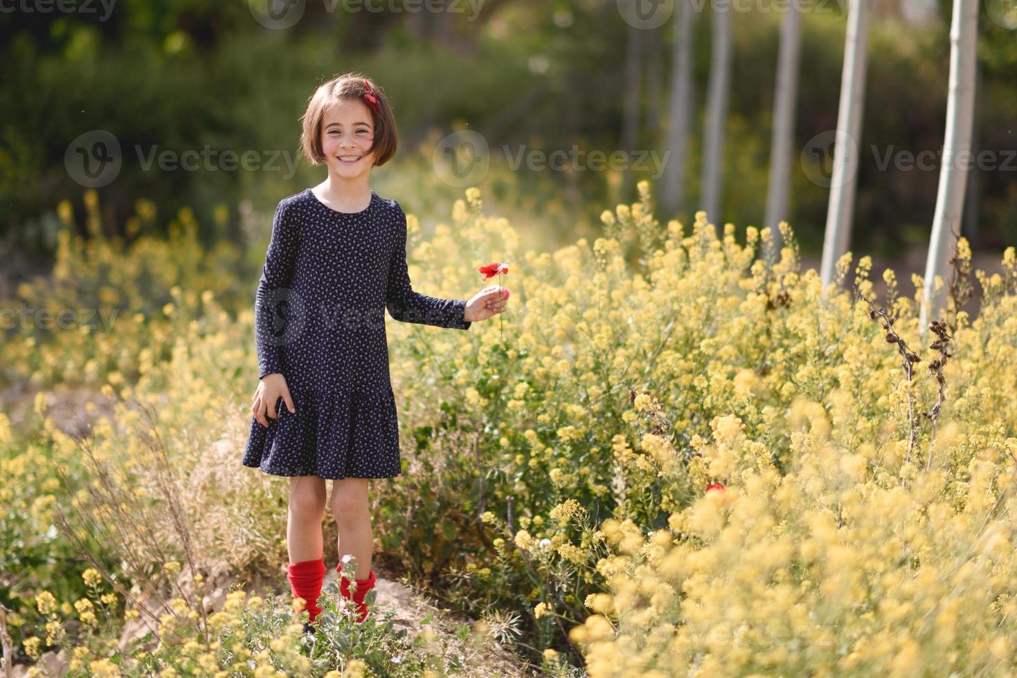 kleines Mädchen, das auf dem Naturfeld spazieren geht und ein schönes Kleid trägt foto