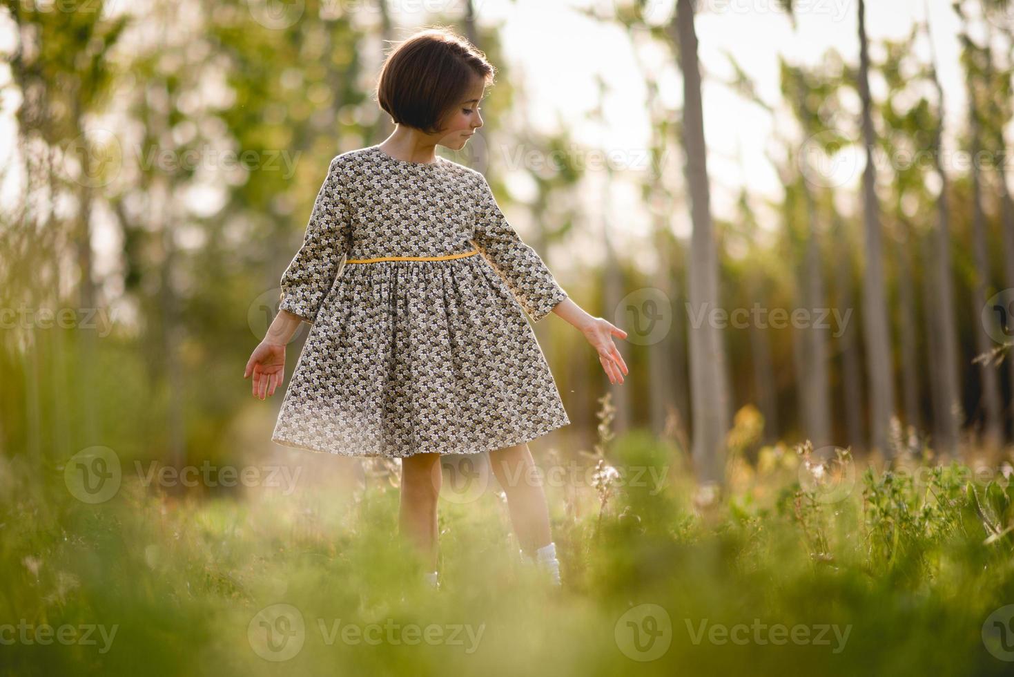 kleines Mädchen im Naturfeld, das ein schönes Kleid trägt foto