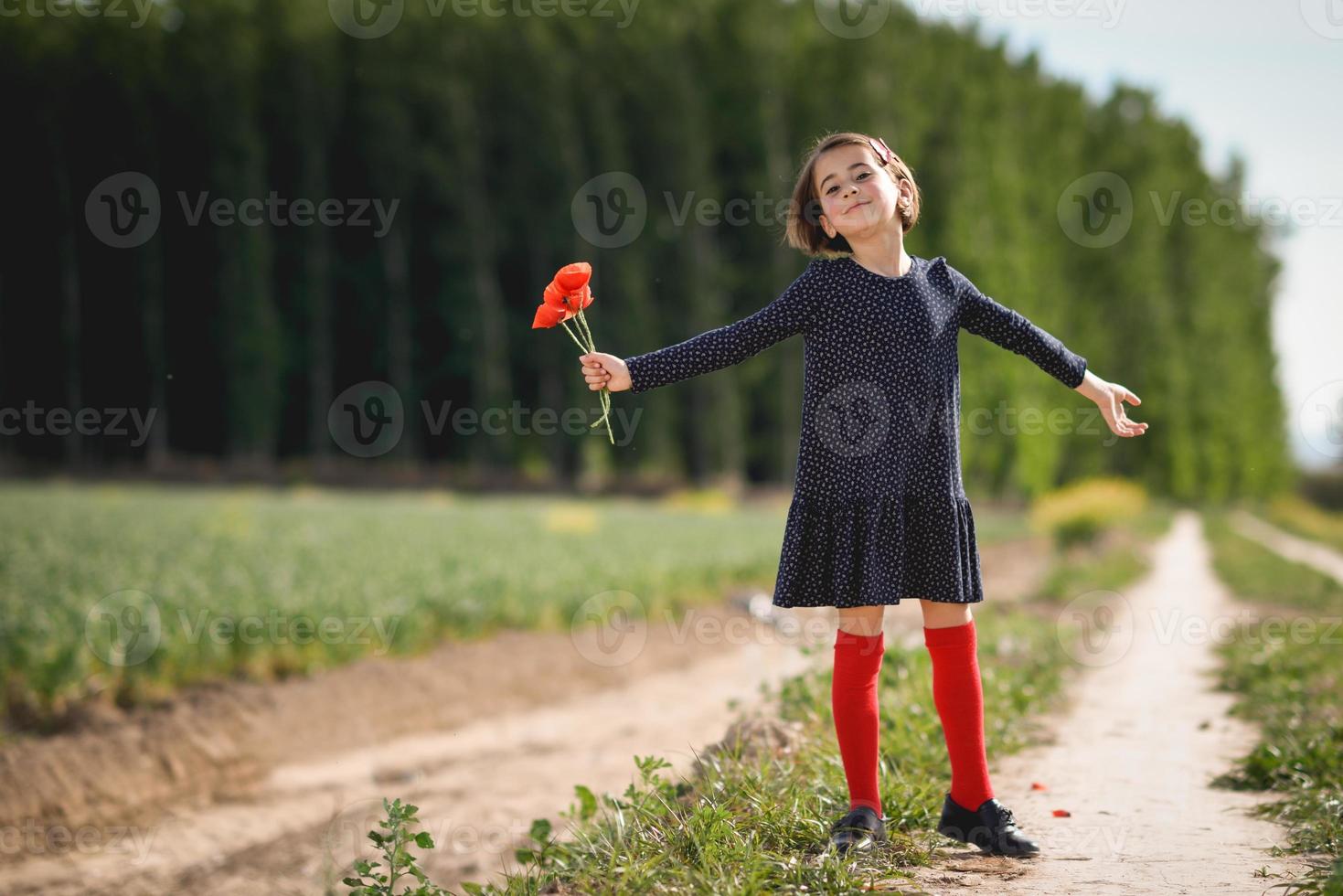 kleines Mädchen, das auf dem Naturfeld spazieren geht und ein schönes Kleid trägt foto