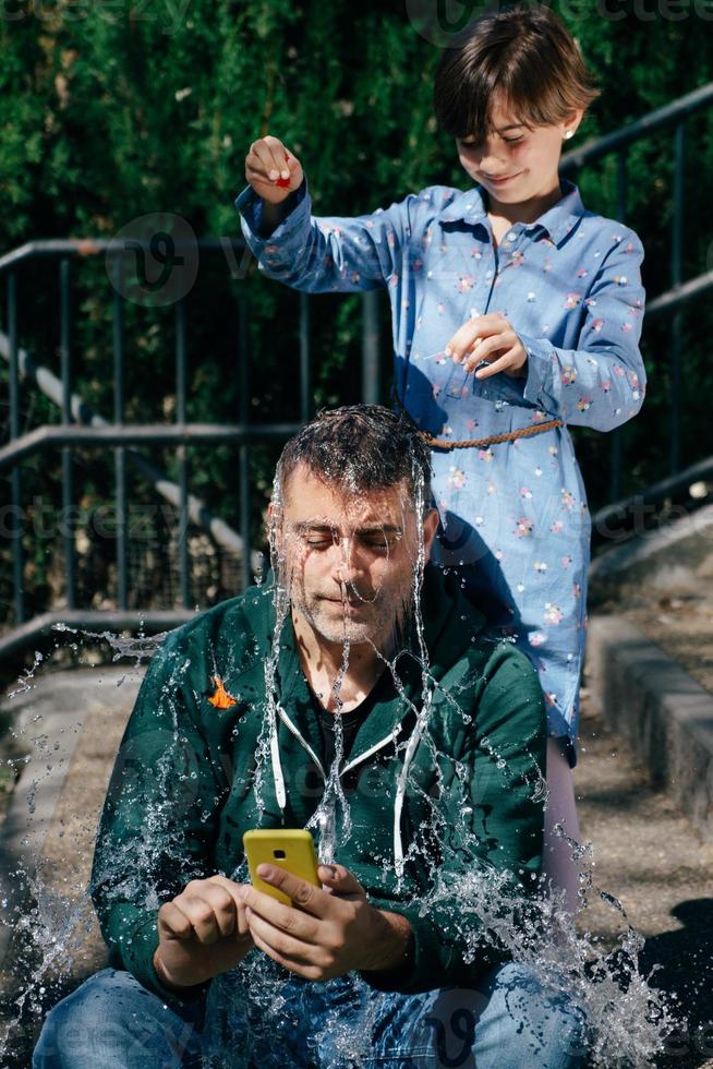 Mädchen bläst einen mit Wasser gefüllten Ballon über dem Kopf ihres Vaters auf foto