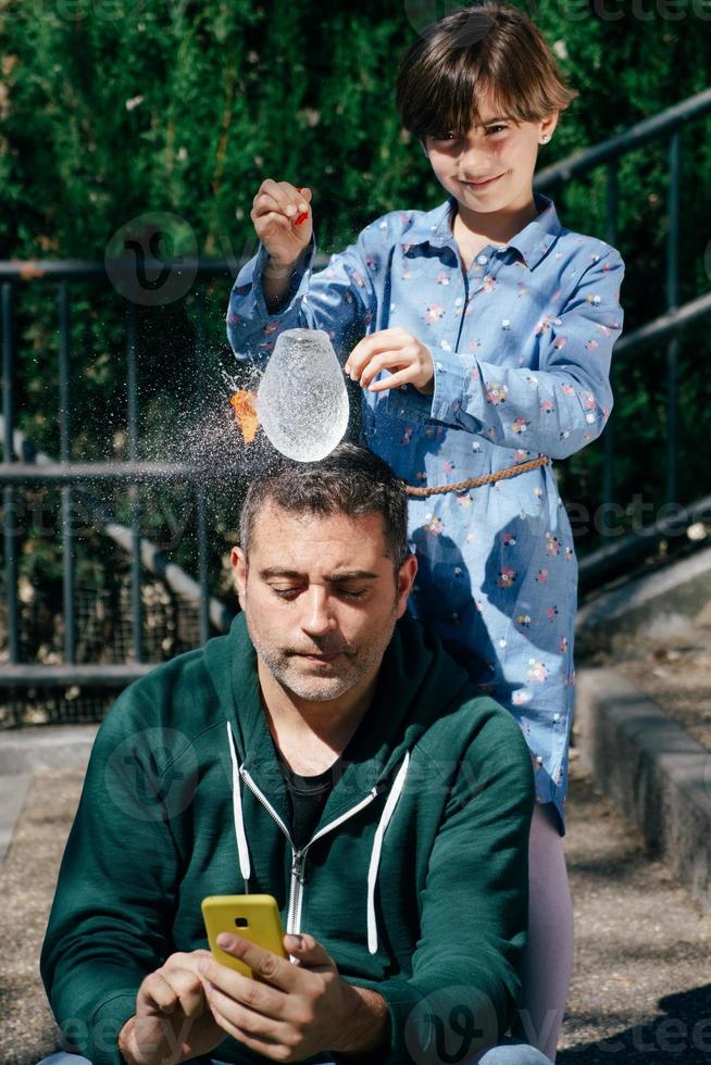 Mädchen bläst einen mit Wasser gefüllten Ballon über dem Kopf ihres Vaters auf foto