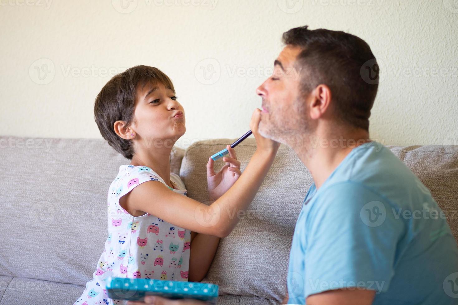 kleine süße Tochter, die ihren Vater schminkt foto