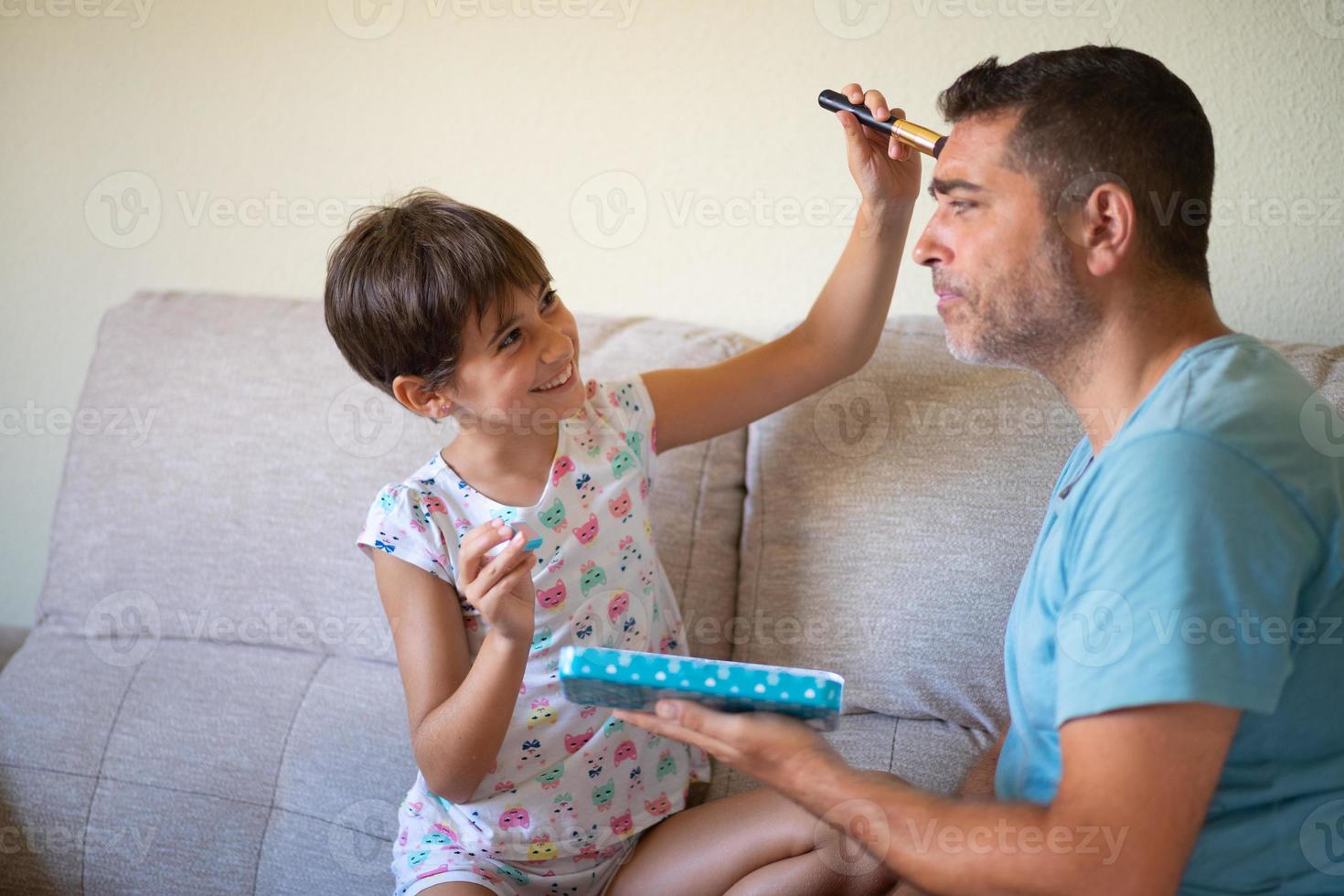 kleine süße Tochter, die ihren Vater schminkt foto