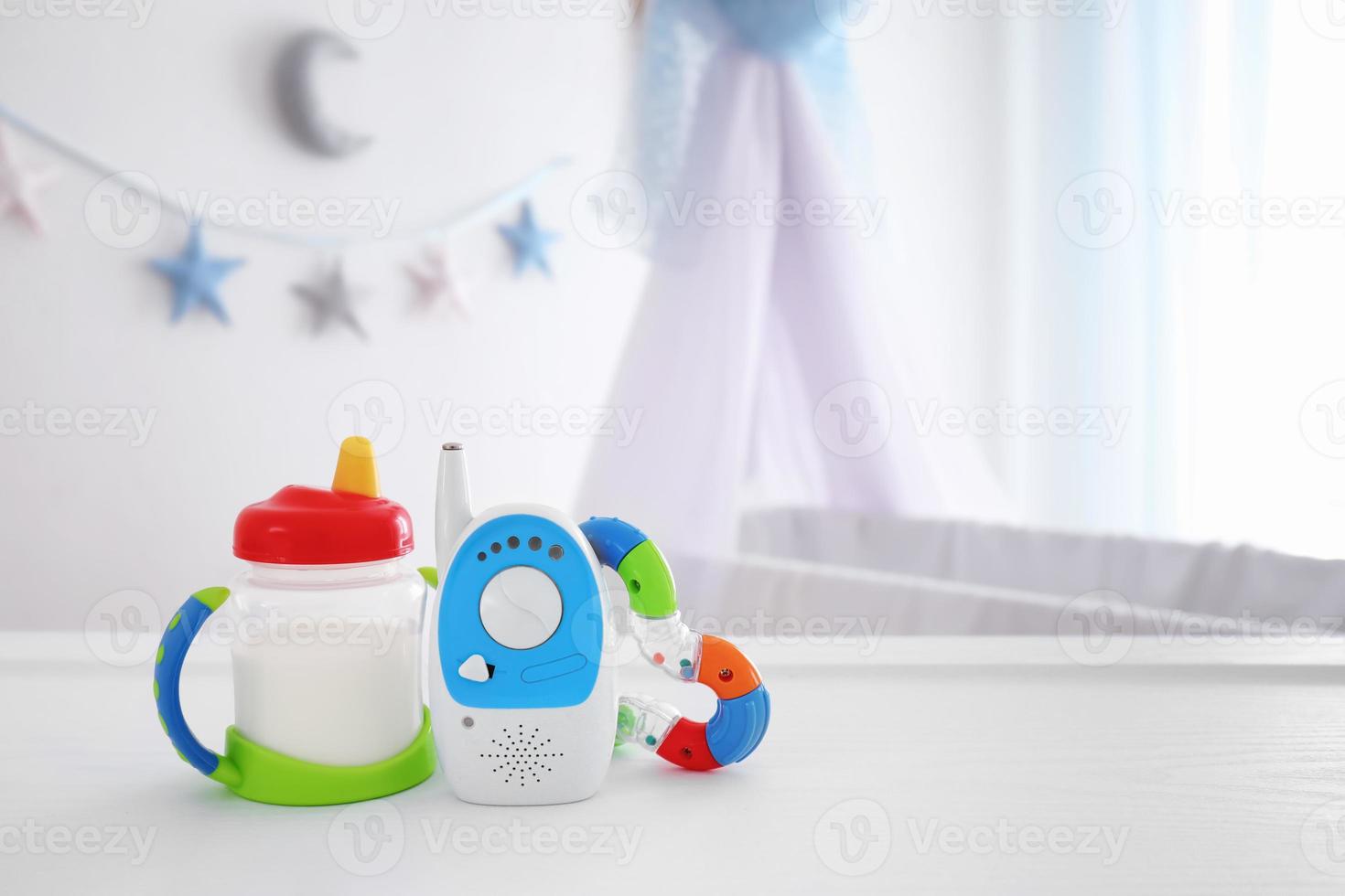 Babyphone, Rassel und Trinkbecher auf dem Tisch im Zimmer. Radio-Kindermädchen foto