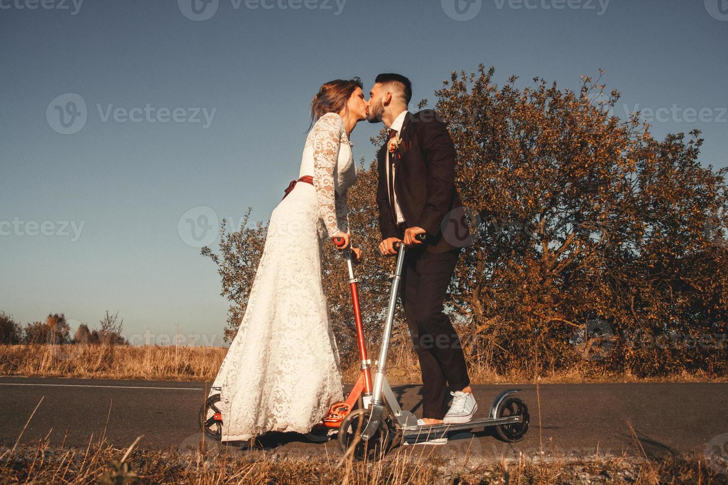 küssendes Hochzeitspaar, das auf Rollern entlang der Straße fährt foto