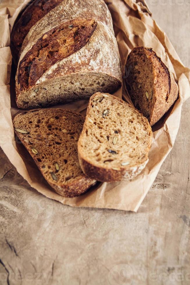 braunes frisches Brot mit Samen werden auf altem Holzhintergrund in Stücke geschnitten foto