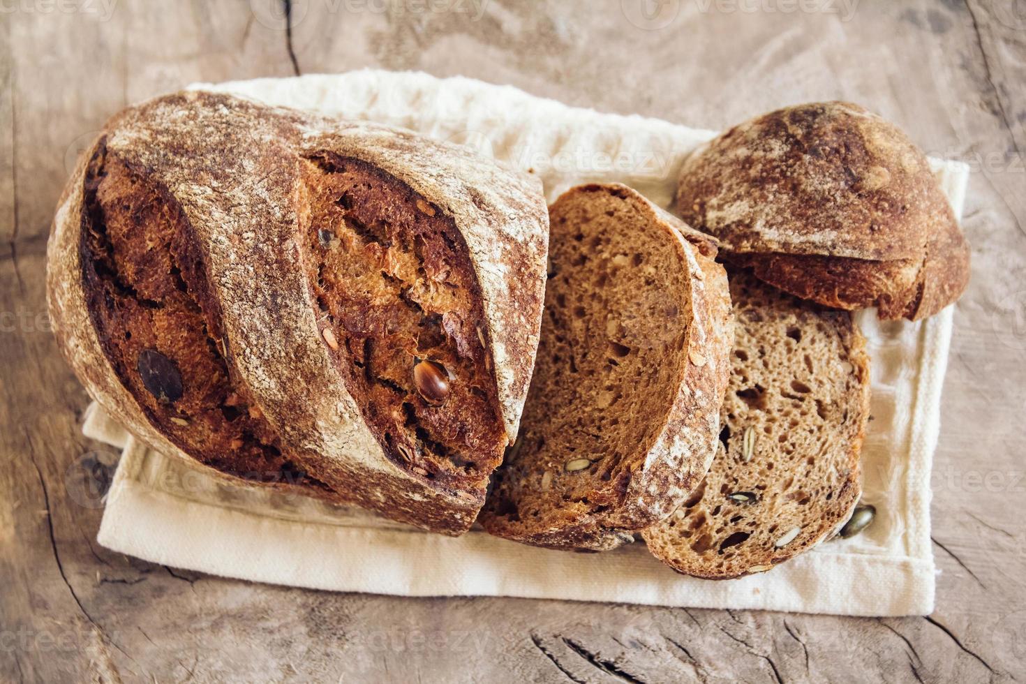 braunes frisches Brot mit Samen werden auf altem Holzhintergrund in Stücke geschnitten foto