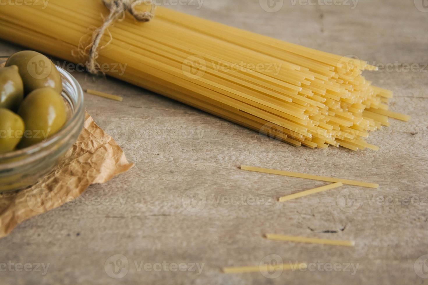 lange gelbe rohe Spaghetti und grüne Oliven auf Holzuntergrund foto