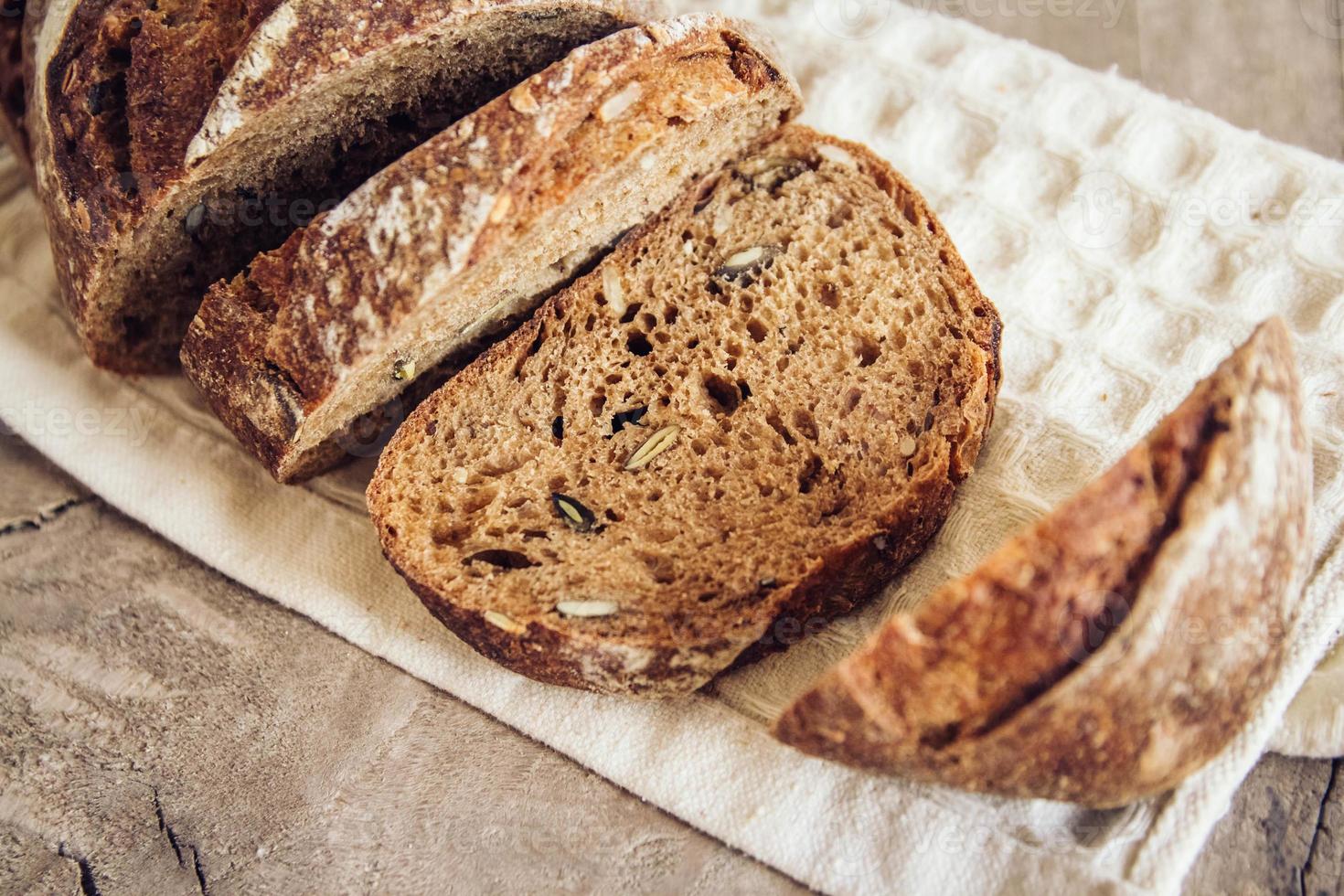 braunes frisches Brot mit Samen werden auf altem Holzhintergrund in Stücke geschnitten foto