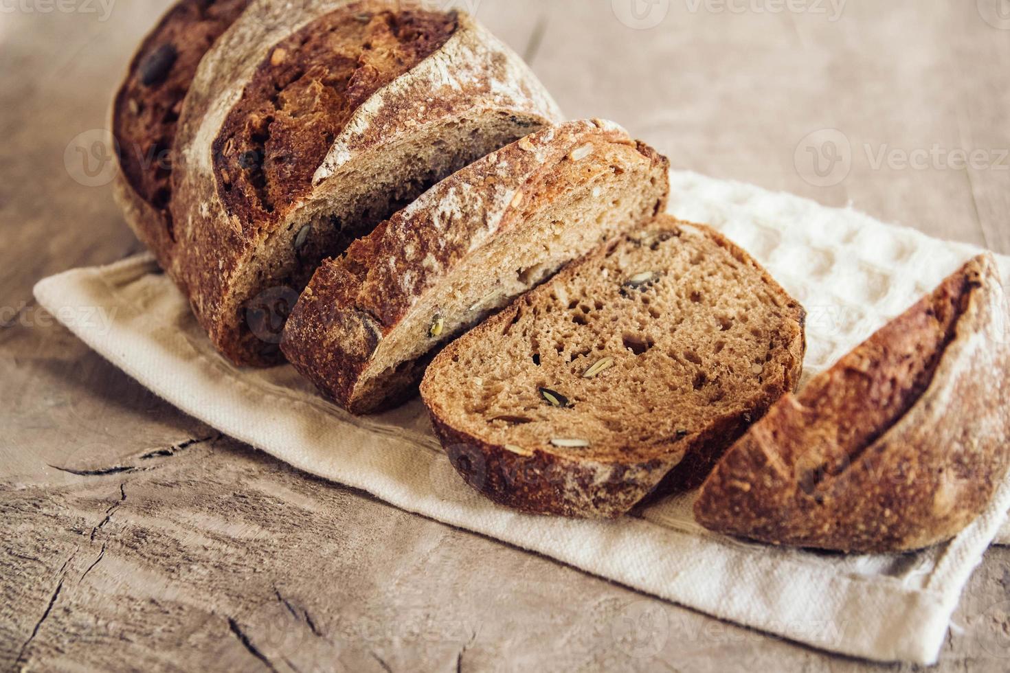 braunes frisches Brot mit Samen werden auf altem Holzhintergrund in Stücke geschnitten foto