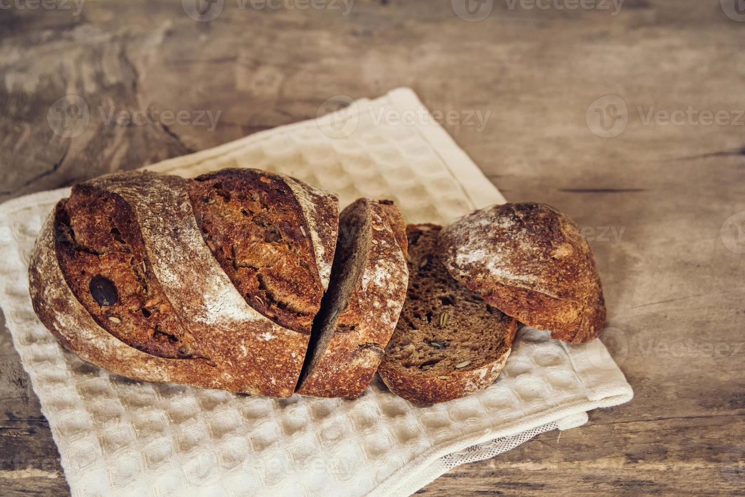 braunes frisches Brot mit Samen werden auf altem Holzhintergrund in Stücke geschnitten foto