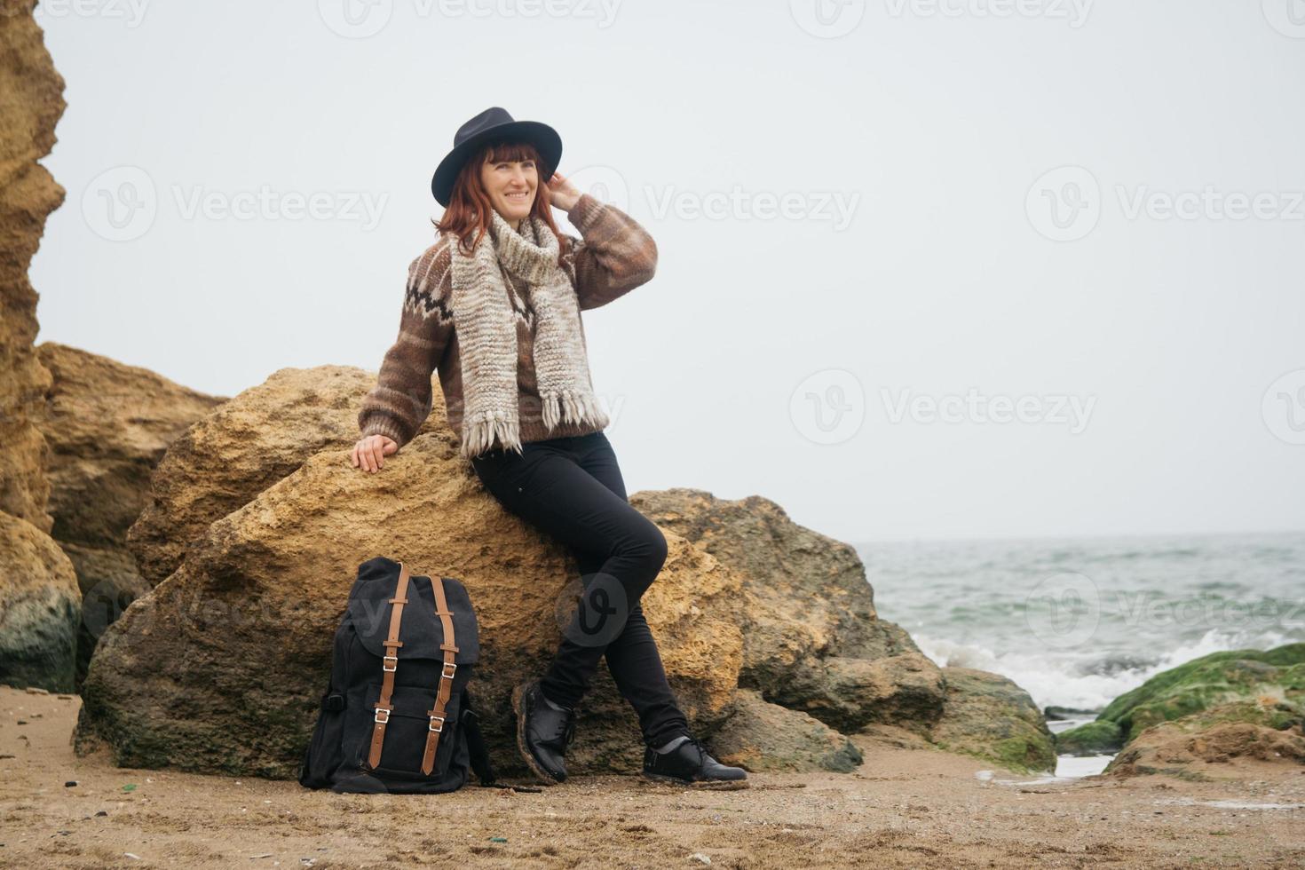 Frau mit Hut und Schal mit Rucksack vor dem Hintergrund von Felsen und schönem Meer foto