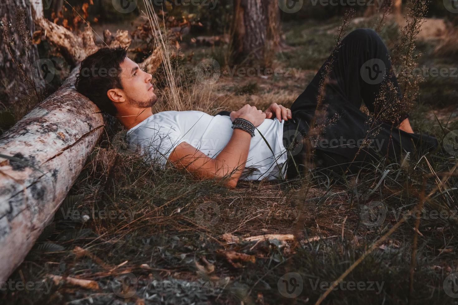 Mann liegt auf Gras und ruht seinen Kopf auf einem Baumstamm mitten im Wald entspannend foto