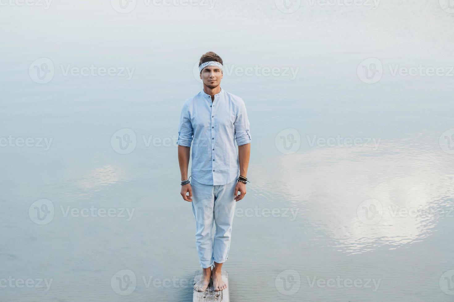 Mann steht auf Holzbrücke und schaut auf den Wasserreflex des blauen Himmels foto