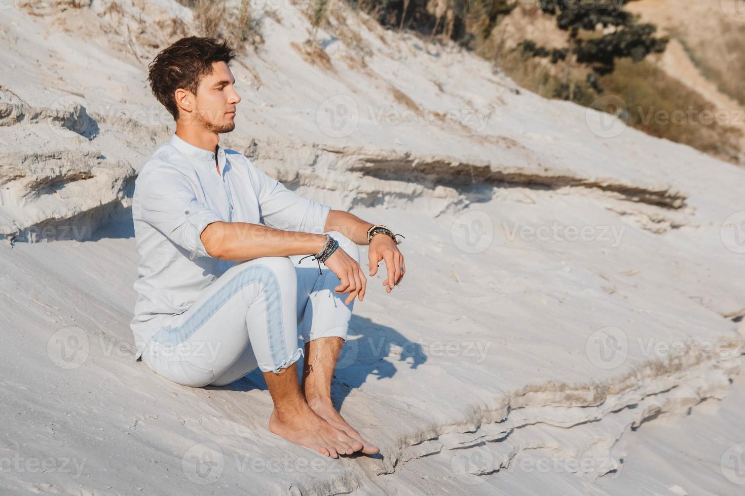 Mann in leichter Kleidung sitzt in der Wüste foto