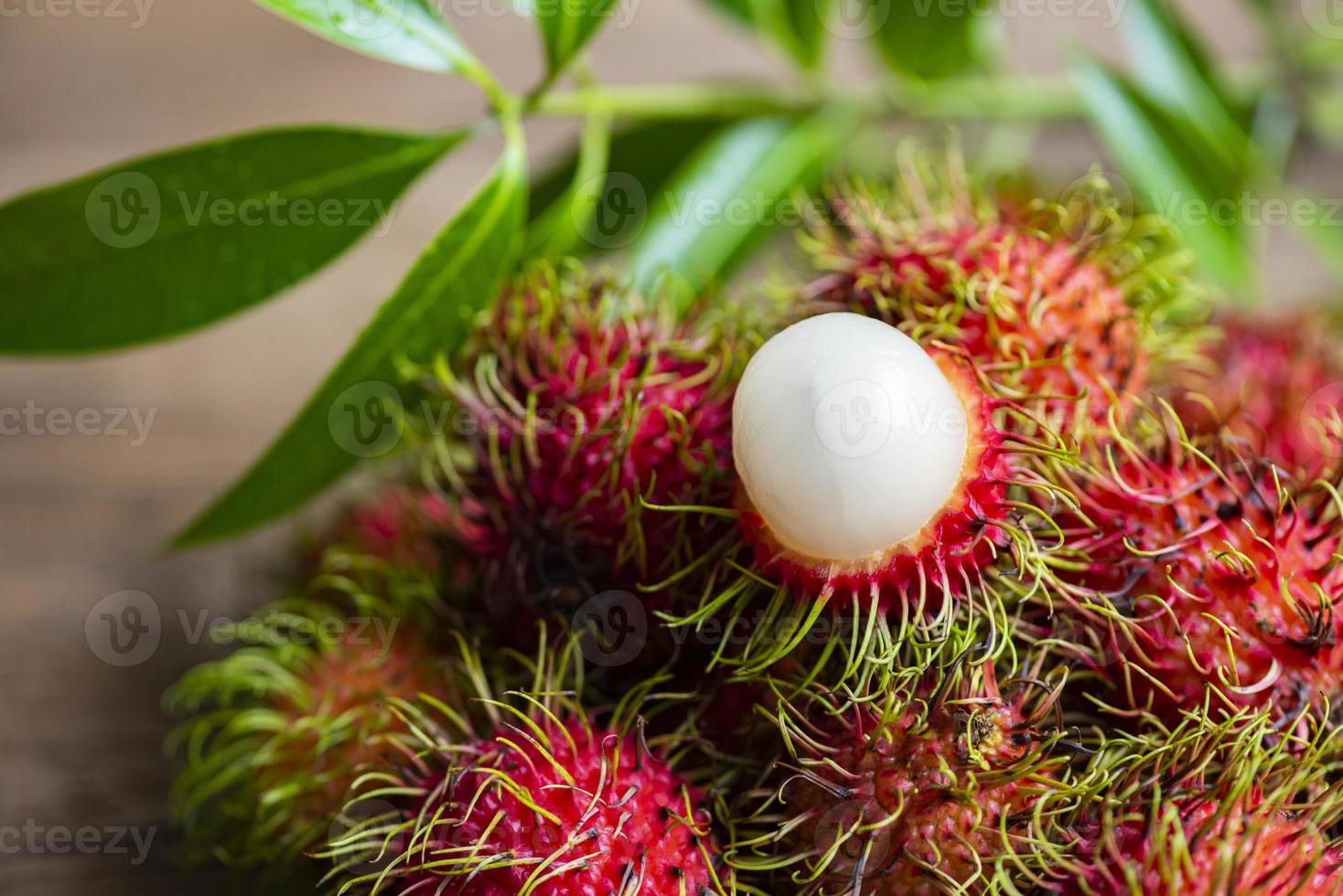 frisches und reifes Rambutan süße tropische Früchte geschältes Rambutan mit Blättern, Rambutanfrucht auf Holzuntergrund Ernte aus dem Garten foto