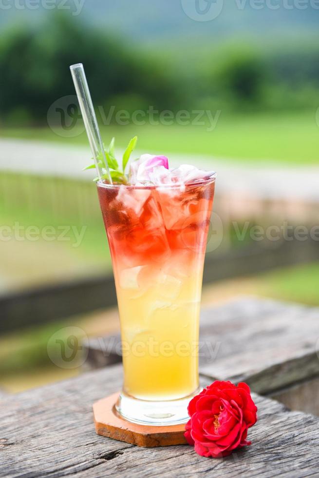 Teeblüten aus Teerosenblättern in einem Glas auf Holztisch und naturgrünem Hintergrund - Eistee mit einem kalten Teerosencocktail foto