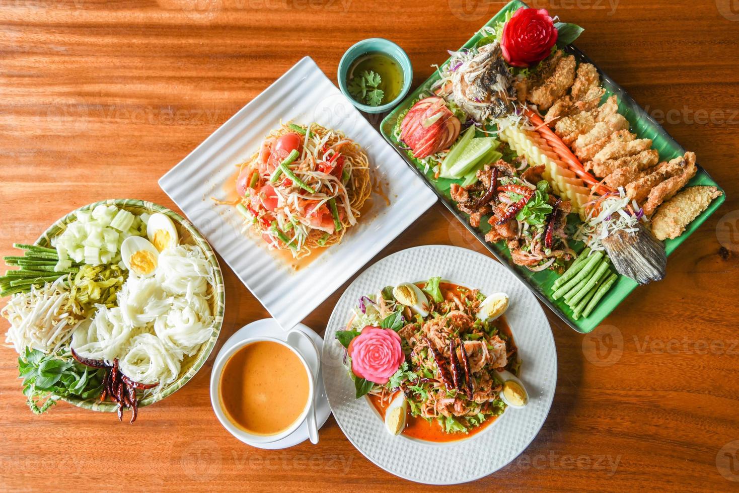 Asiatisches thailändisches Essen Draufsicht mit thailändischem Reisnudeln Curry, Papayasalat, Garnelensalat und Salatfischessen serviert auf Holztischplatte foto
