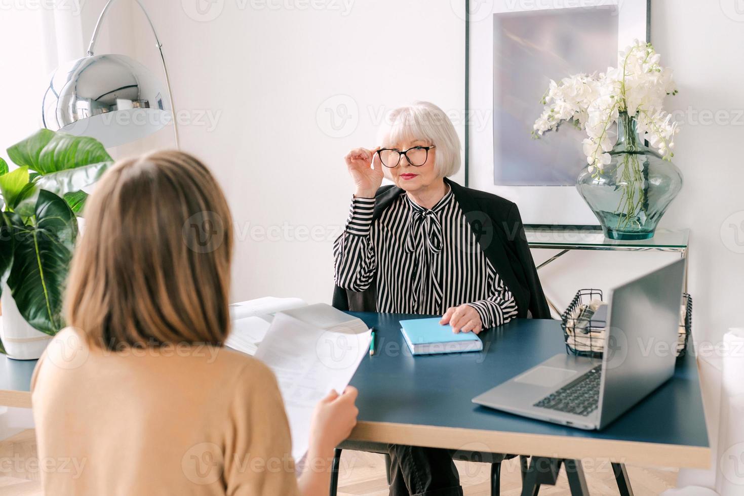 Ältere stilvolle Frau mit junger Frau, die Arbeitsaufgaben im Büro bespricht. Geschäft, Kommunikation, Arbeit, Alter, Zusammenarbeit, Mentoring-Konzept foto