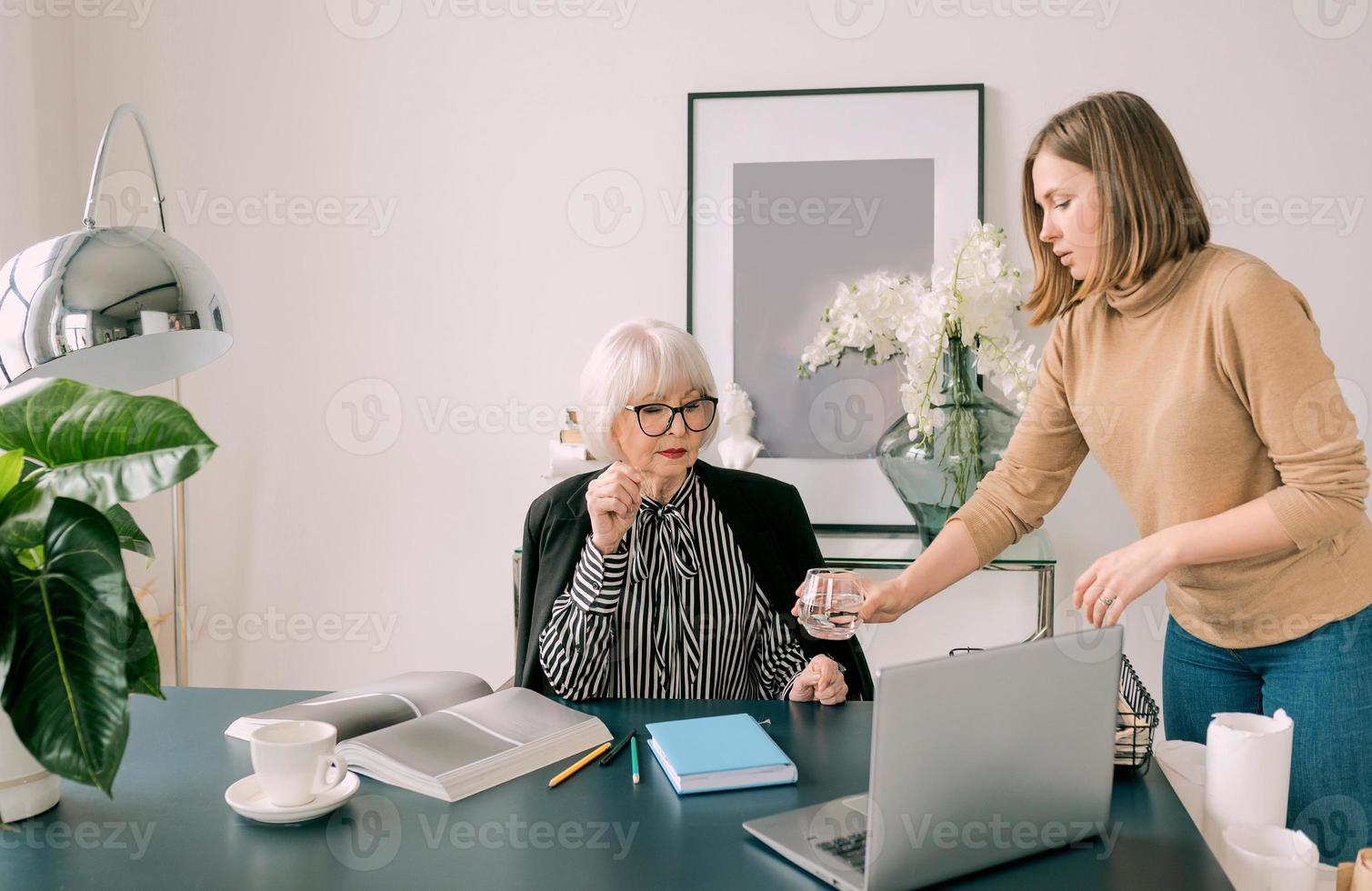 Der junge Assistent brachte dem Chef im Büro ein Glas Wasser. Geschäft, Kommunikation, Arbeit, Alter, Zusammenarbeit, Mentoring-Konzept foto