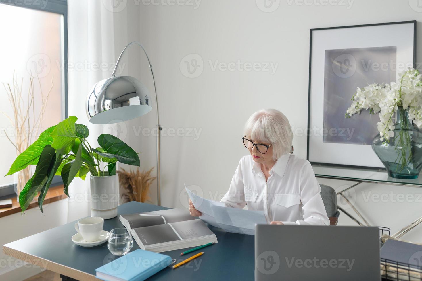 müde senior schöne graue haare frau in weißer bluse lesen dokumente im büro. Arbeit, Senioren, Probleme, Lösung finden, Konzept erleben foto