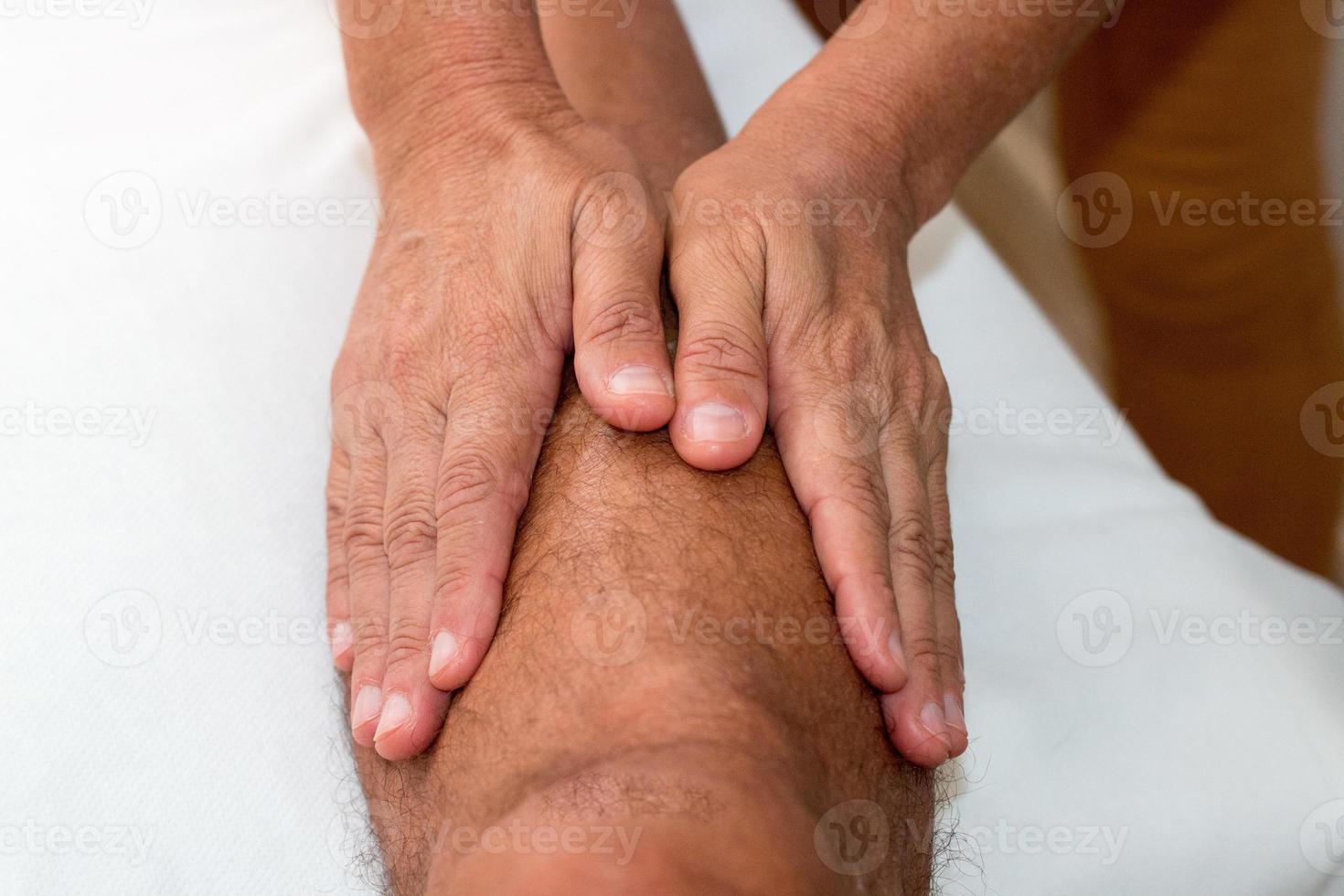 Massagetherapeut massiert das Bein eines Mannes unterhalb des Knies foto