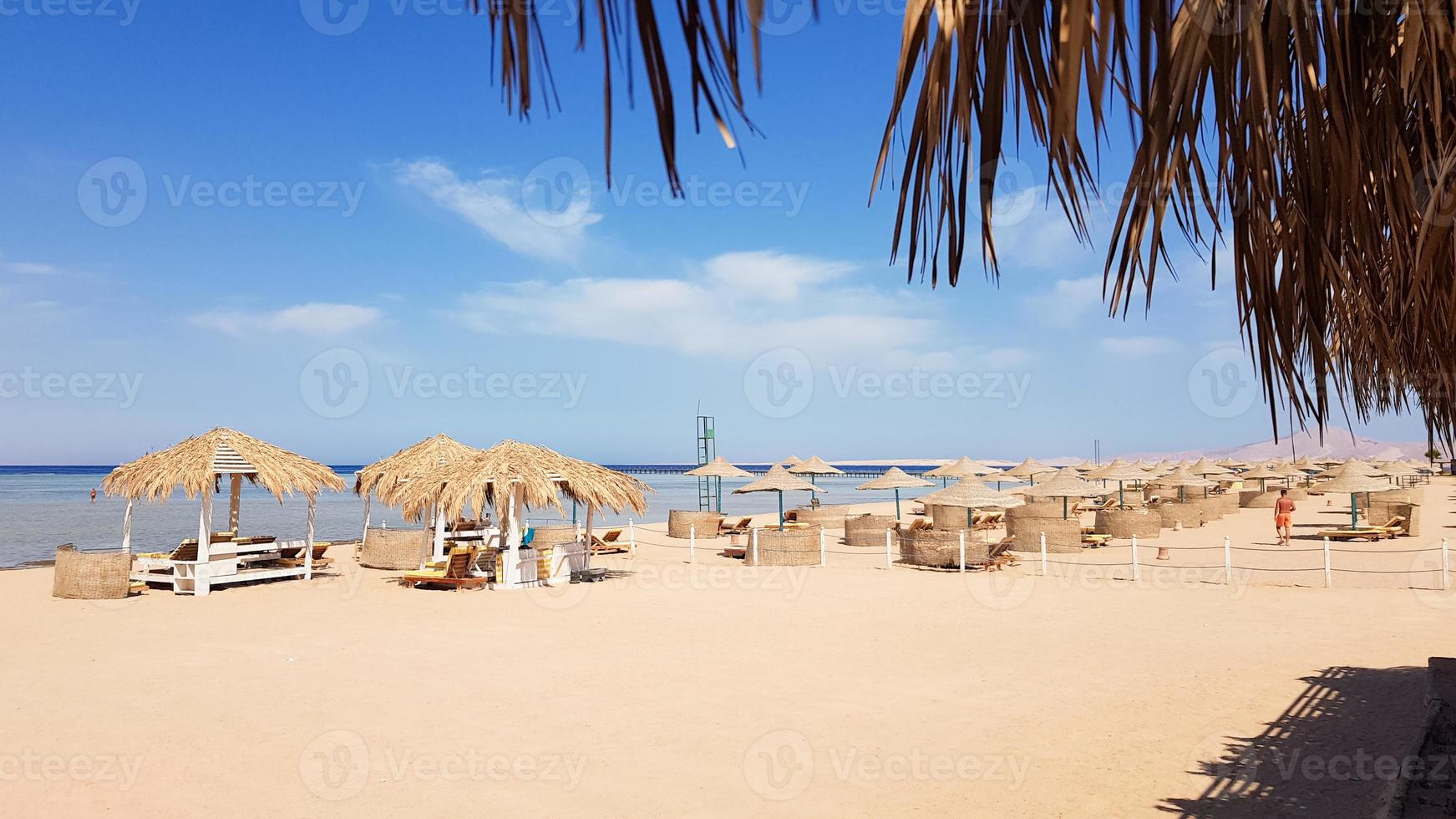 Ein wunderschöner tropischer Strand mit strohgedeckten Sonnenschirmen am Ufer des Roten Meeres in Sharm el Sheikh. Sommerlandschaft schöner sonniger Strand in Ägypten. das Konzept von Urlaub, Reisen, Urlaub foto