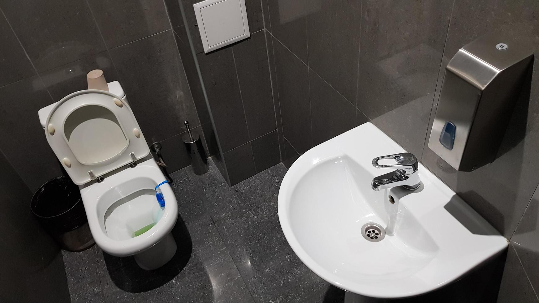 weißes Keramikwaschbecken mit verchromter Armatur in der Toilette mit grauer Kachel foto