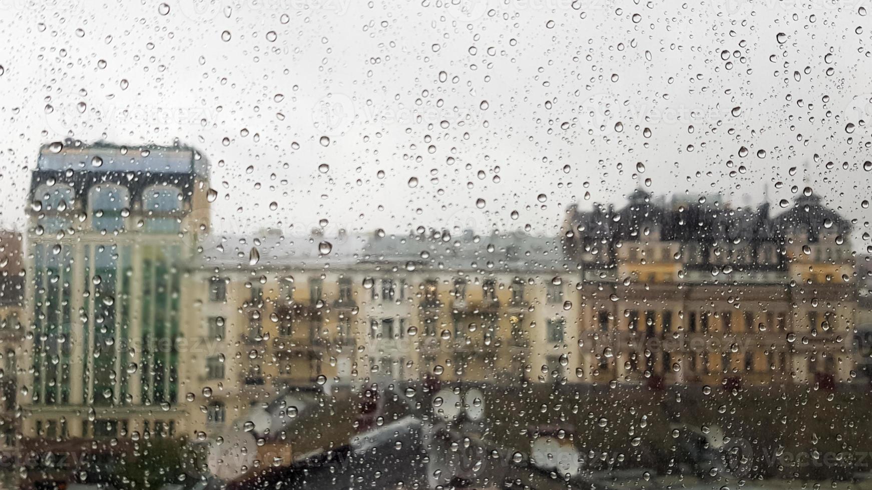 nasses Fenster mit Tropfen auf dem Hintergrund der Herbststadt bei bewölktem Wetter. Blick aus dem Fenster im Regen. Wassertropfen auf Glasfenster bei Regen mit unscharfem Hintergrund der Stadtszene foto