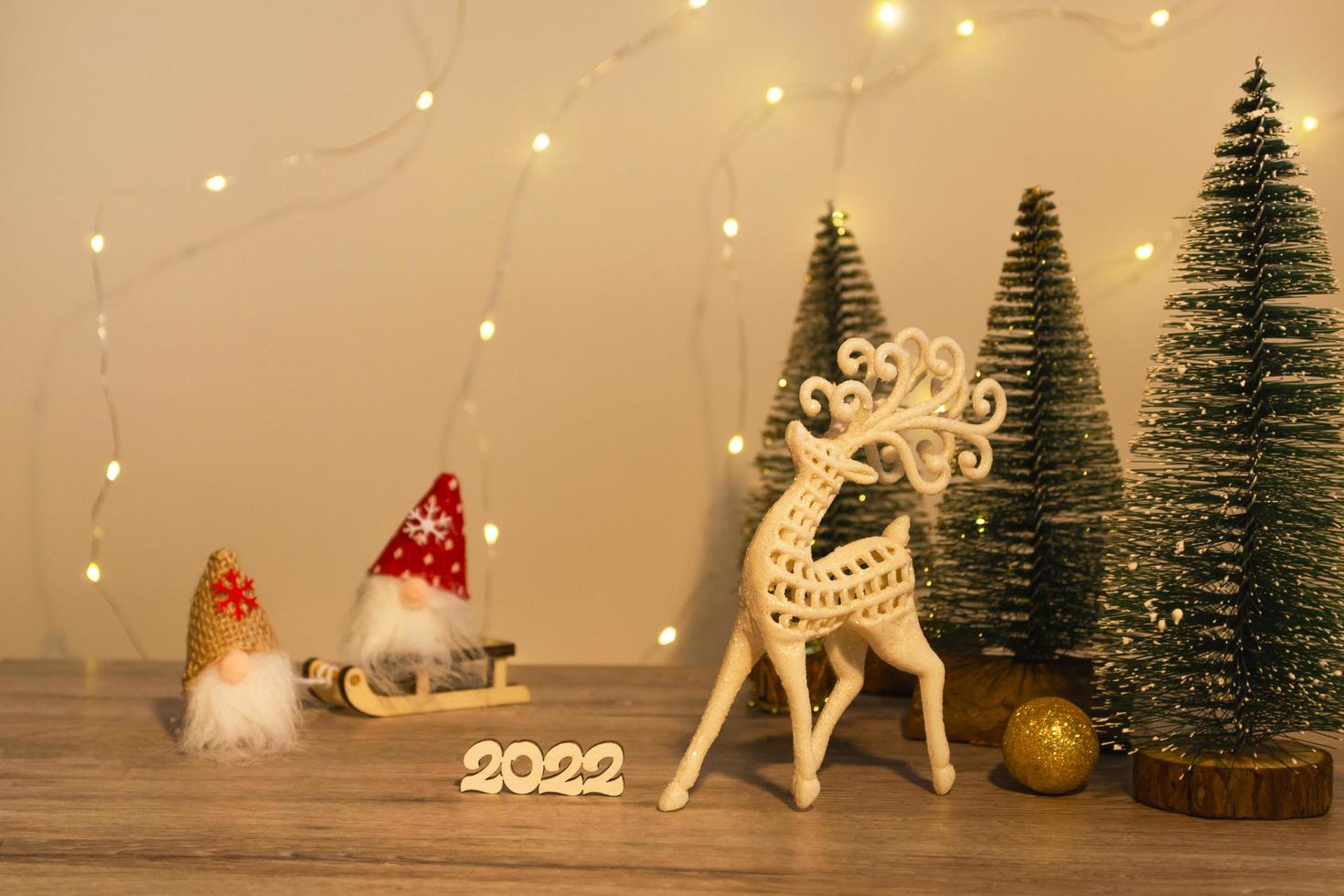 Weihnachts- und Neujahrsdekoration. Weihnachtshirsch, Zahlen 2022, Gnome auf einem Schlitten und Weihnachtsbäume auf einem hölzernen Hintergrund mit Lichtern. Weihnachtskarte foto