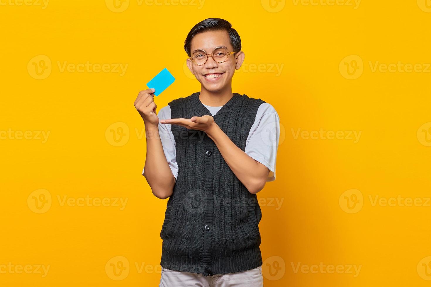 Fröhlicher asiatischer Mann, der eine leere Karte mit der Handfläche zeigt, die auf gelbem Hintergrund isoliert ist foto