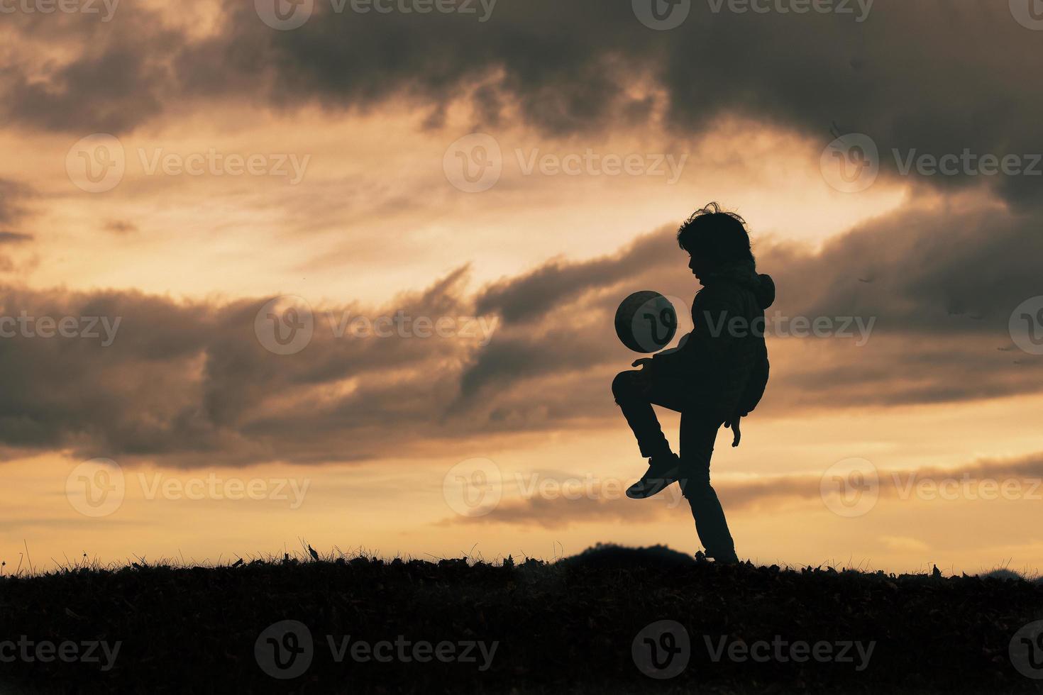 Kind in Silhouette dribbelt und spielt mit Fußball foto
