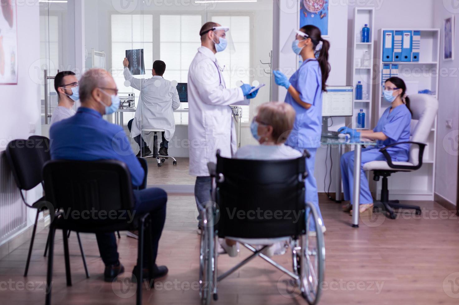 medizinisches Team mit Visier und Schutzmaske bespricht das Stehen im Wartezimmer foto