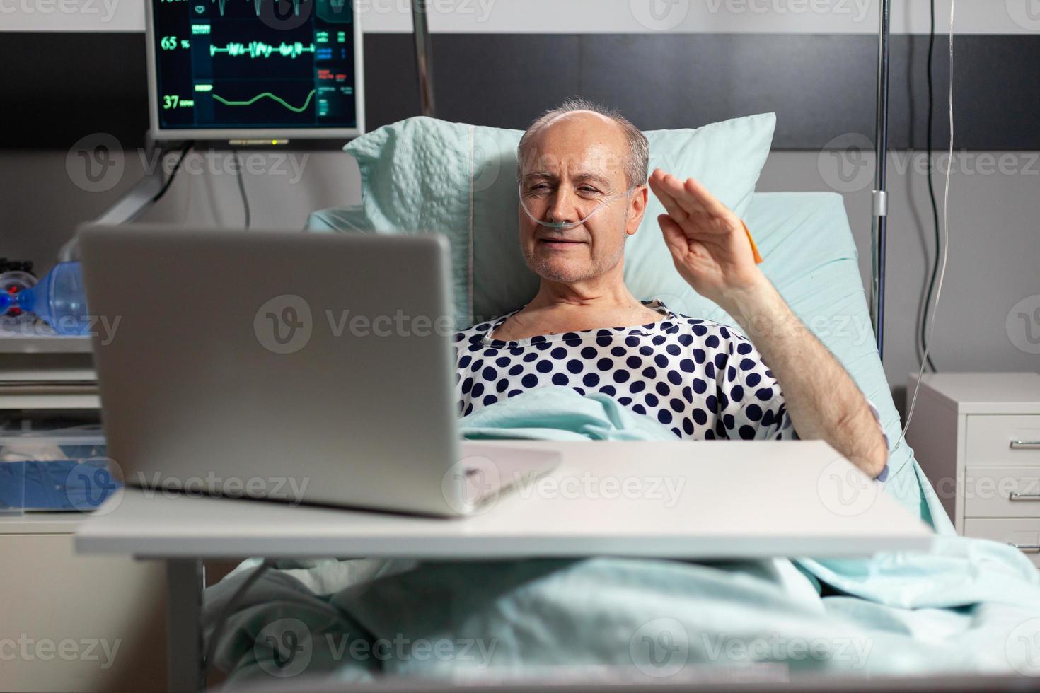 Porträt eines älteren Mannes, der die Familie begrüßt, die auf die Laptop-Kamera winkt foto