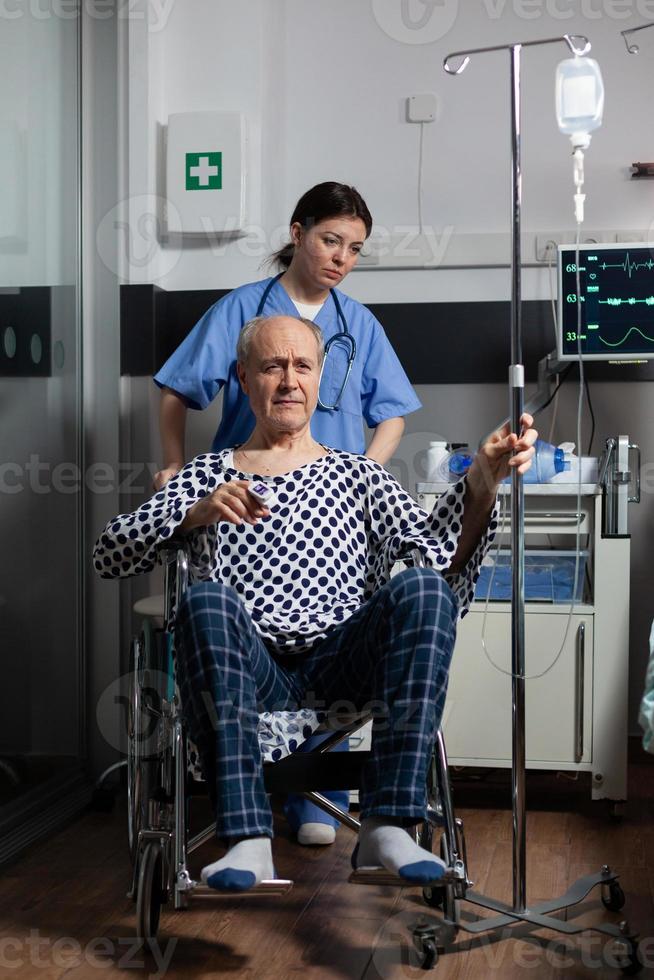 im Krankenhaus eingelieferter älterer Mann, der im Rollstuhl im Krankenzimmer sitzt foto