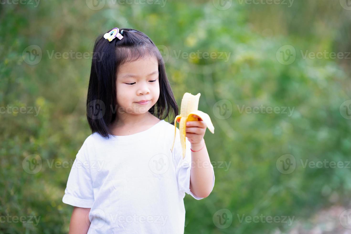 glückliches Kind genießt es, gelbe Banane zu essen. asiatisches Mädchen süßes Lächeln. foto