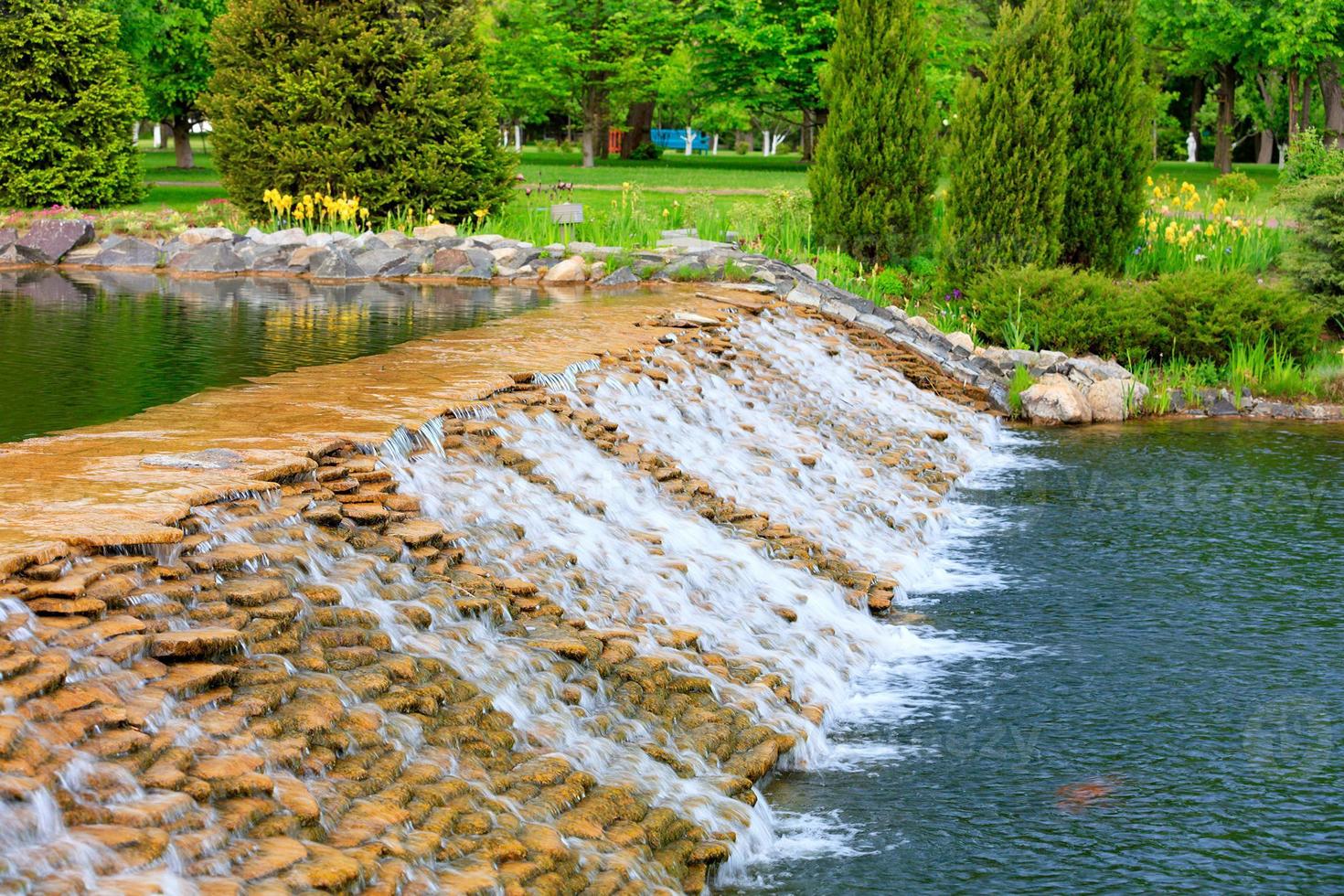 das Wasser eines schönen dekorativen Wasserfalls fließt schnell in einen Sommerpark. foto