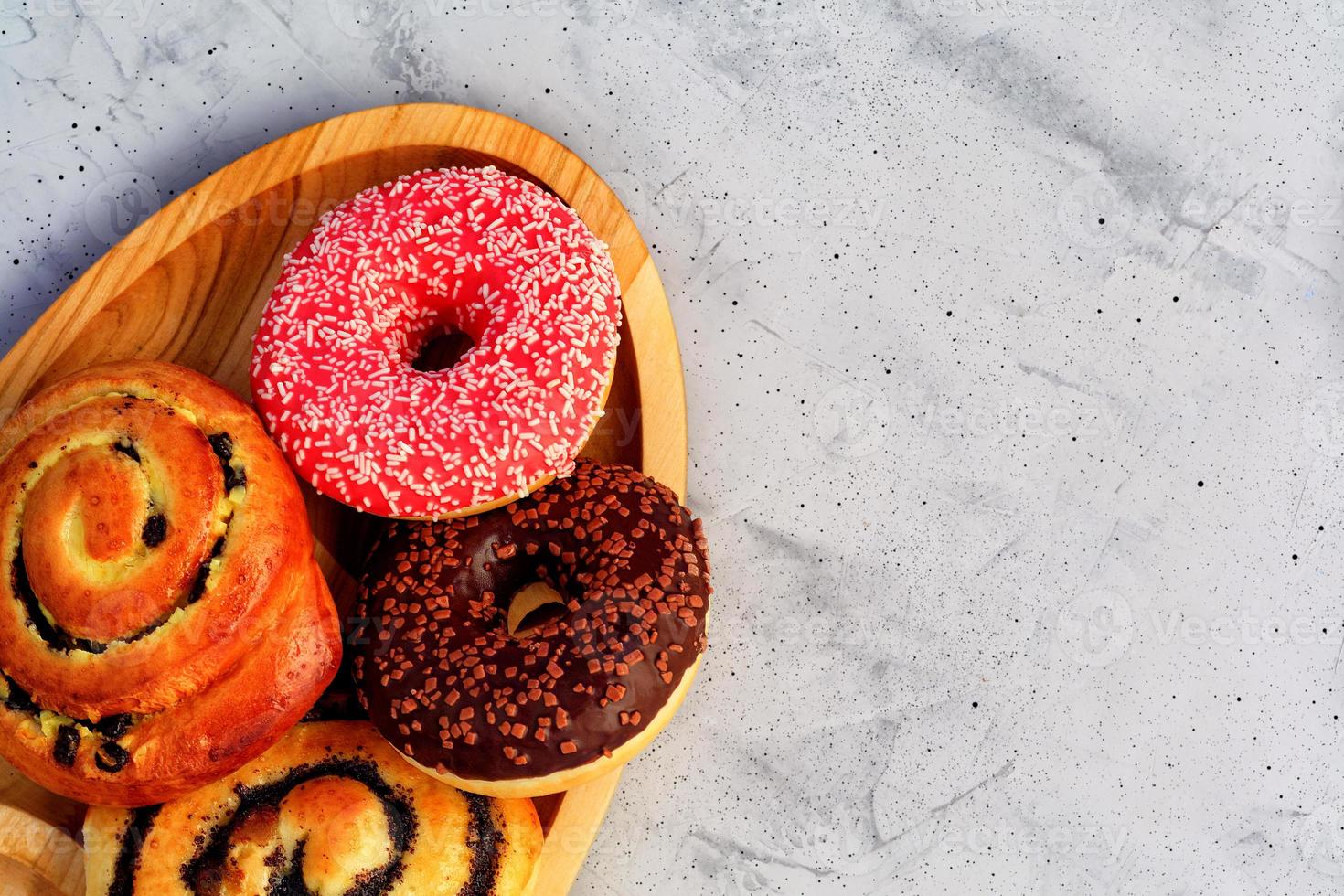 Auf einem ovalen Holztablett und einer grauen Betonoberfläche liegen leckere Schoko-Donuts und -Brötchen mit Mohn und Rosinen. foto