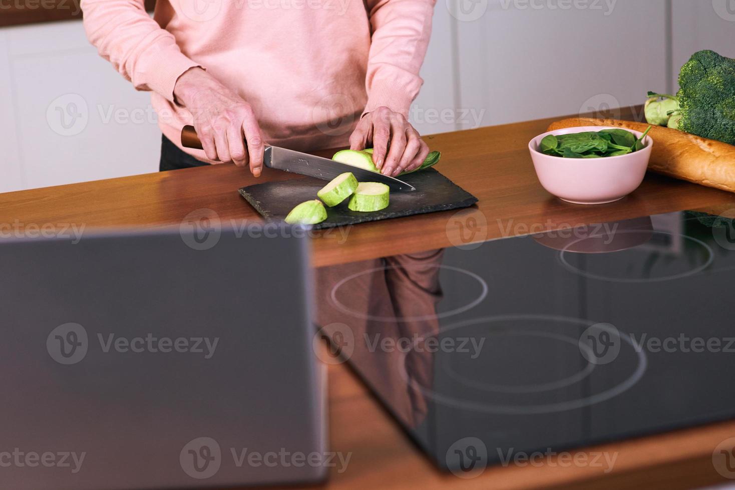 Senior fröhliche Frau kocht in der modernen Küche mit dem Laptop. Essen, Bildung, Lifestyle-Konzept foto